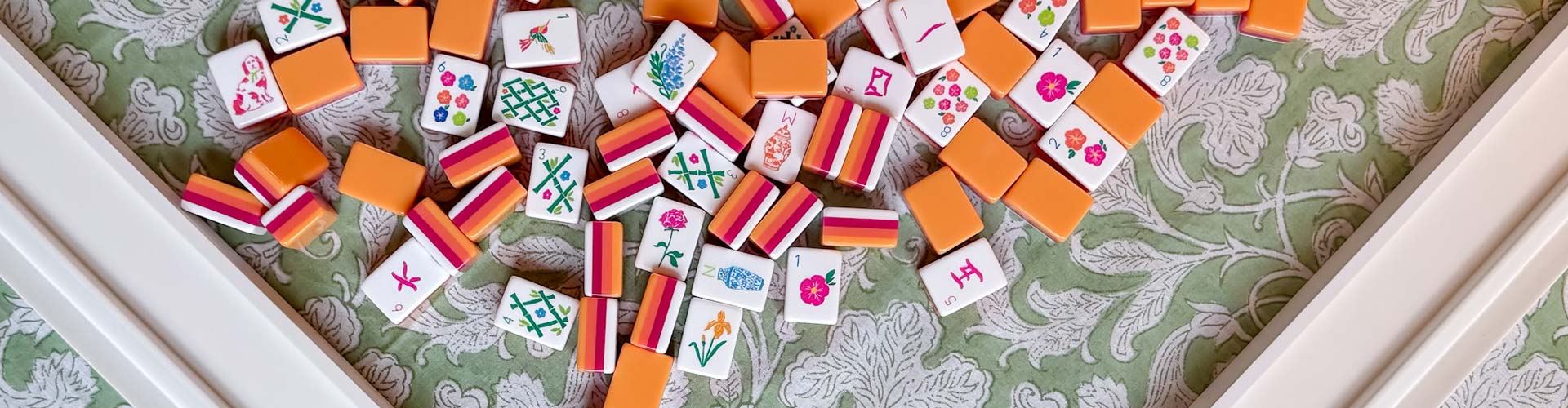 Beautiful colorful mahjong tiles scattered on a lovely tablecloth with mahjong racks and pushers visible