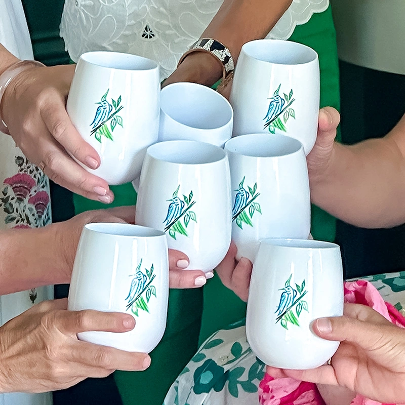 Close up of the ladies of Mahjong & Magnolias toasting with their Tervis x M&M collaboration stemless glasses. The drinkware is white and features the Mahjong & Magnolias signature bird bam artwork.